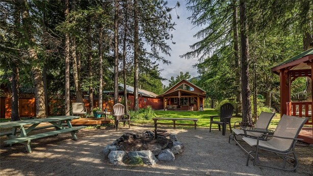 Une cabane avec un foyer, une table de pique-nique et des chaises longues, située dans un cadre forestier.