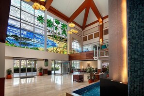 A spacious lobby with a large glass wall, a pool, and a high ceiling with wooden beams.