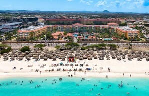 A resort with a large beach area, multiple pools, and a prominent hotel building with a red roof.