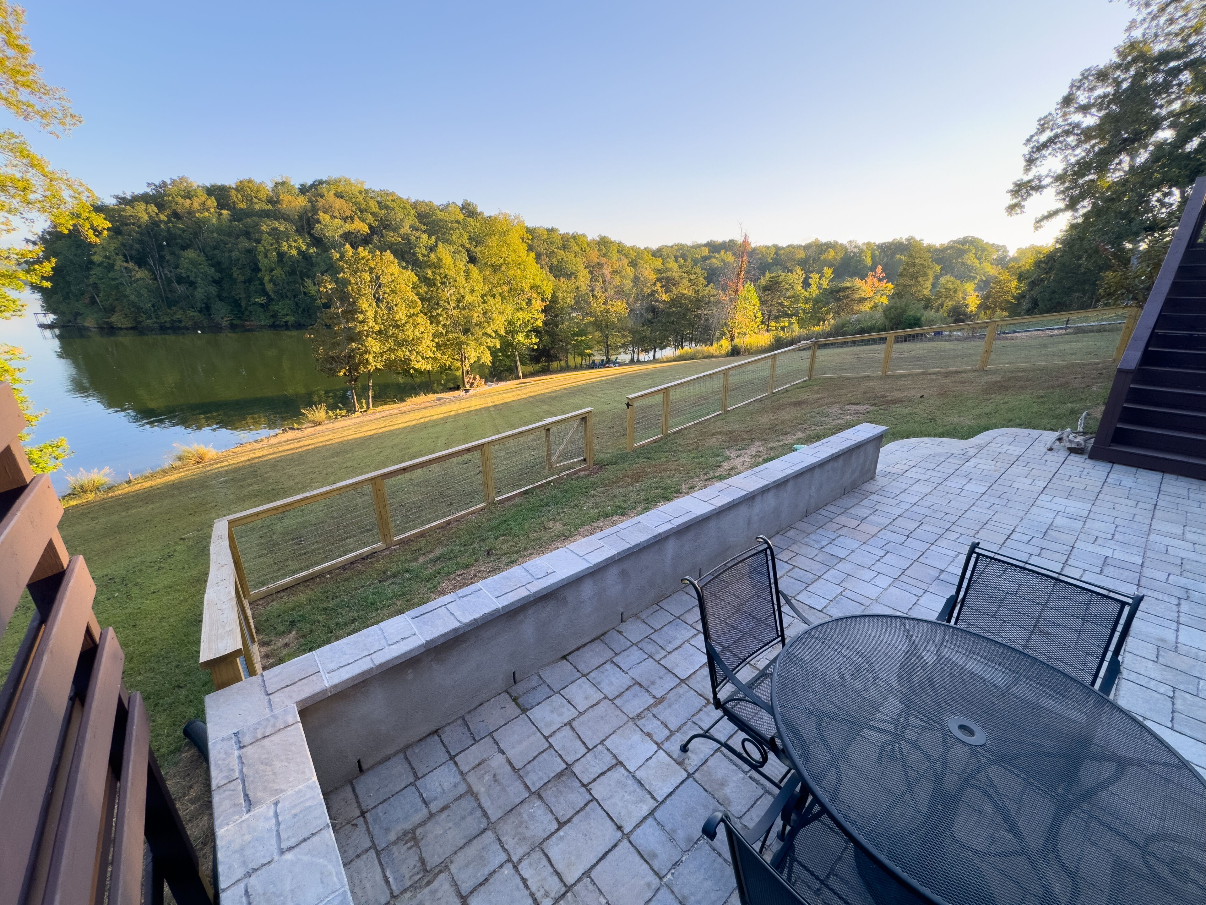 A patio with a table and chairs, overlooking a lake and forested area.