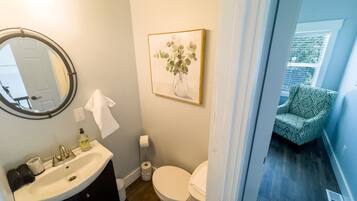 A bathroom with a round mirror, white sink, toilet, and a framed picture on the wall.
