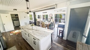 A modern kitchen with a marble island, wooden flooring, and a dining area with a view.