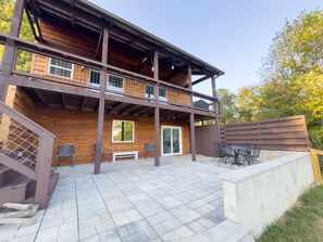 Eine zweistöckige Holzhütte mit einer Terrasse, Sitzgelegenheiten im Freien und Blick auf die umliegenden Bäume.