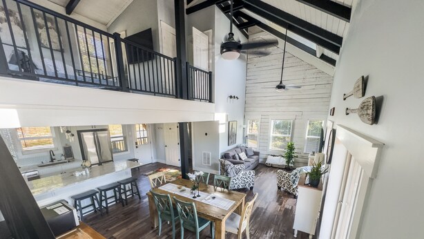 A spacious loft-style living area with a high ceiling, exposed beams, and a mezzanine level.