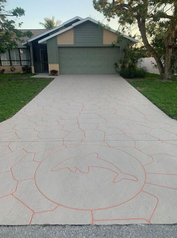 A paved driveway leading to a house with a green garage and a brown roof.
