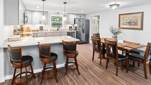 A modern kitchen with a central island, bar stools, a dining table with chairs, stainless steel appliances, and a framed picture on the wall. - NEW LISTING- Riverfront / Unique / Perfect location/ Private  (Lakeview)