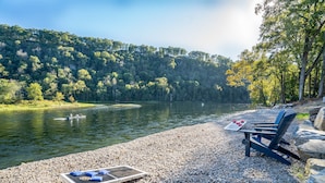 A lakeside view with a pebbled beach, a lounge chair, a sun lounger, and a small boat on the water. - NEW LISTING- Riverfront / Unique / Perfect location/ Private  (Lakeview)
