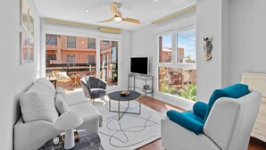 Una sala de estar moderna con sofá, sillón y mesa de centro, ventanas amplias y ventilador de techo.