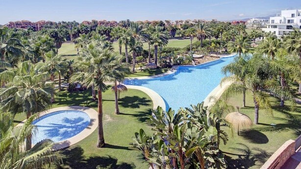 Un resort con una amplia piscina rodeada de palmeras y vegetación.
