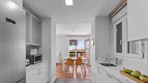 Una cocina moderna con armarios blancos, un comedor con mesa y sillas, y vista al exterior.