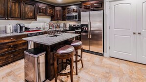 A modern kitchen with dark wood cabinets, stainless steel appliances, a granite countertop, and a central island with bar stools. - 30% OFF, Ski Dream Sleeps 14 in Comfort! 2 Dedicated HotTubs,BBQ,5 Min to Dwntwn (Ogden)