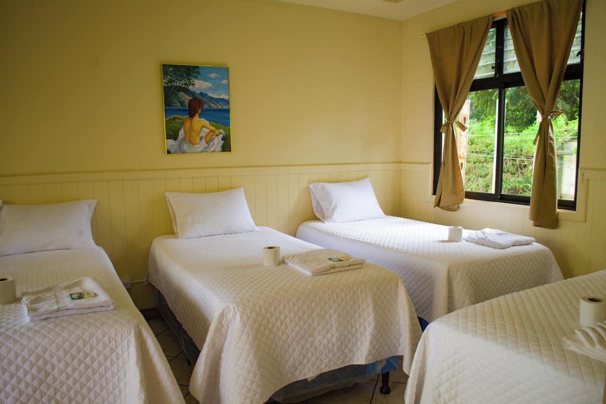 A hotel room with three single beds, a painting on the wall, and a window with curtains.