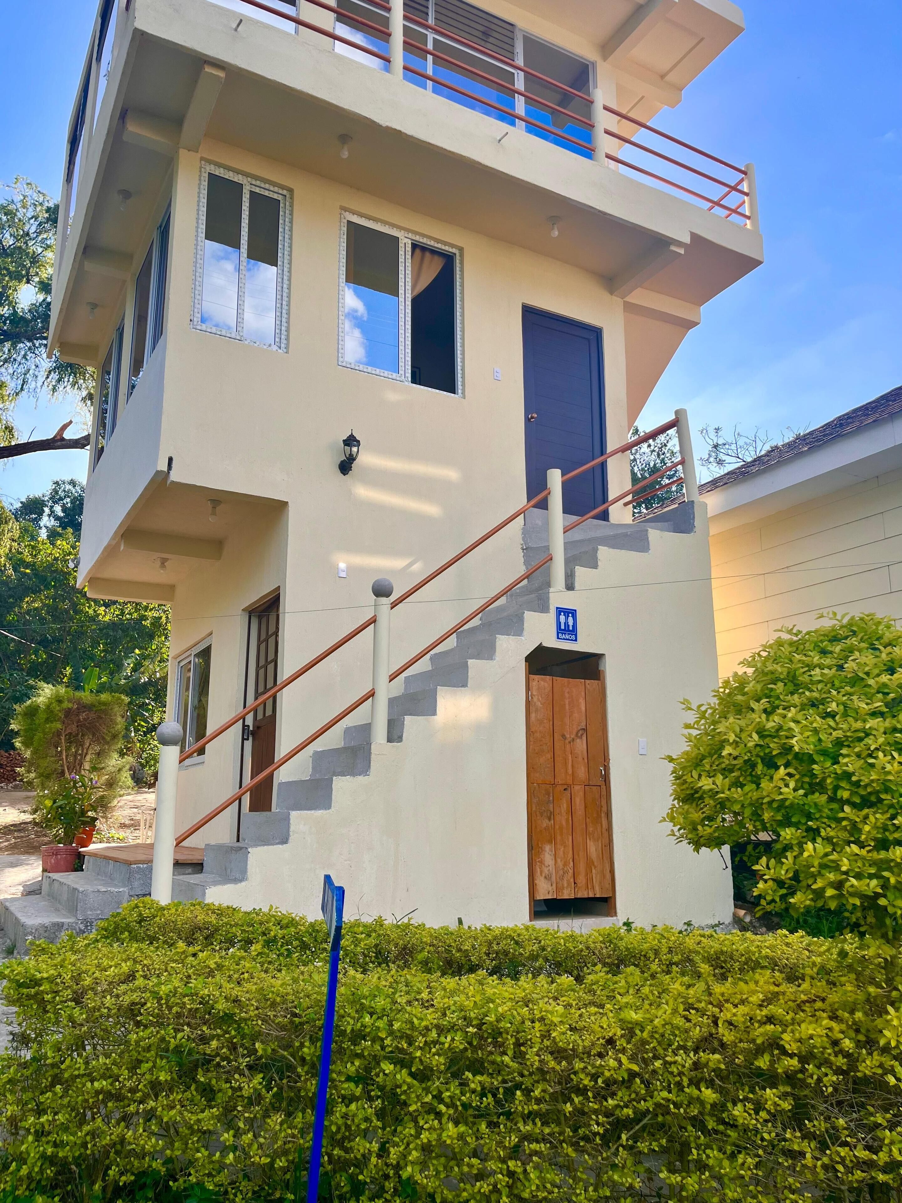 A two-story building with a staircase leading to the upper floor, a blue door, and a sign indicating a bank nearby.