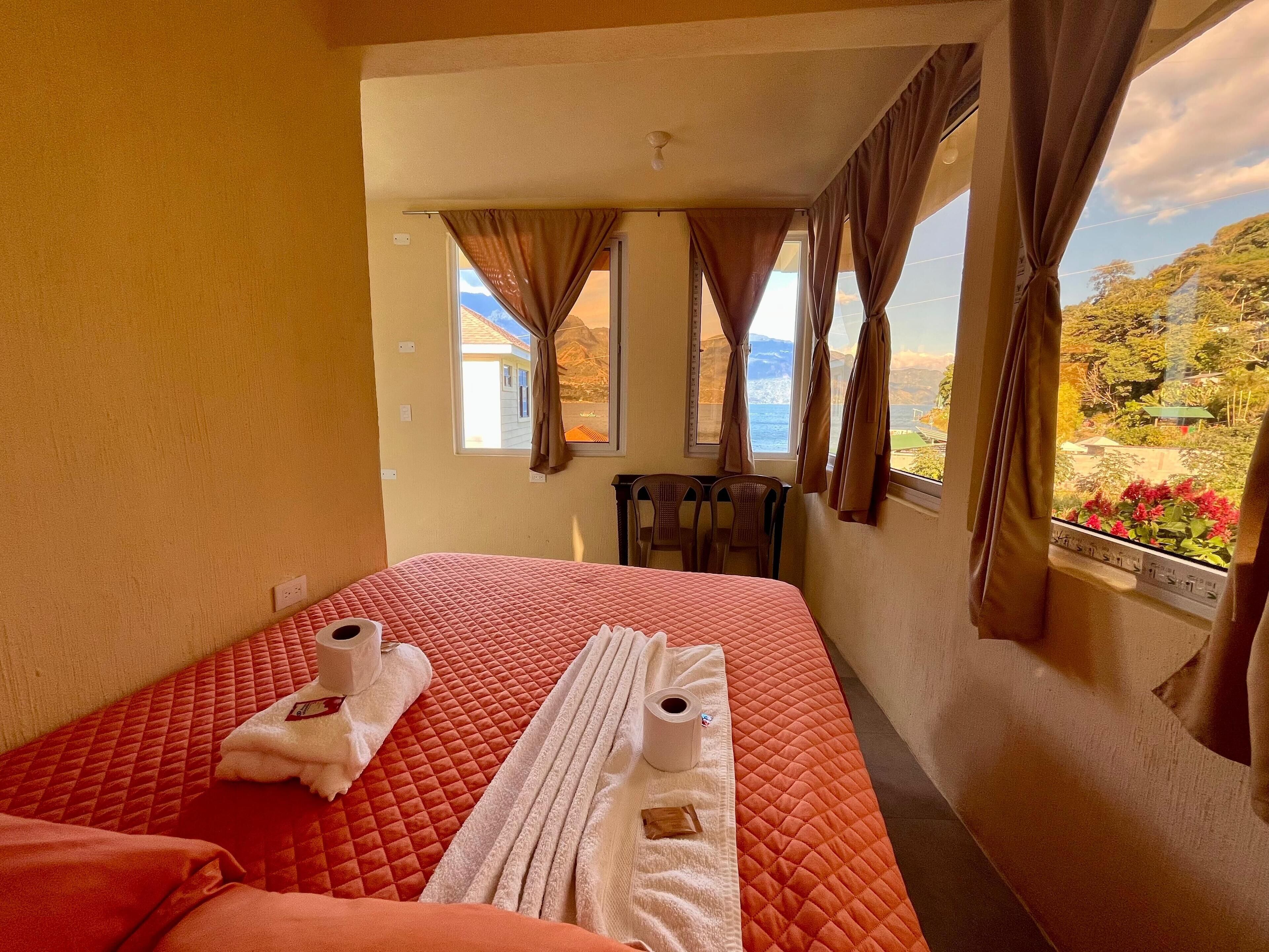 Habitación de hotel con una cama, dos sillas, una mesita y una ventana con cortinas.