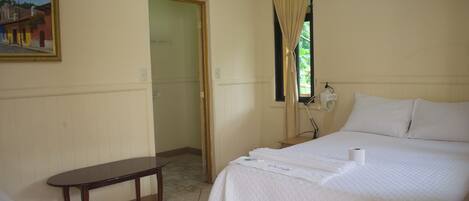 A hotel room with a bed, a bedside table, a painting on the wall, and a window with curtains.