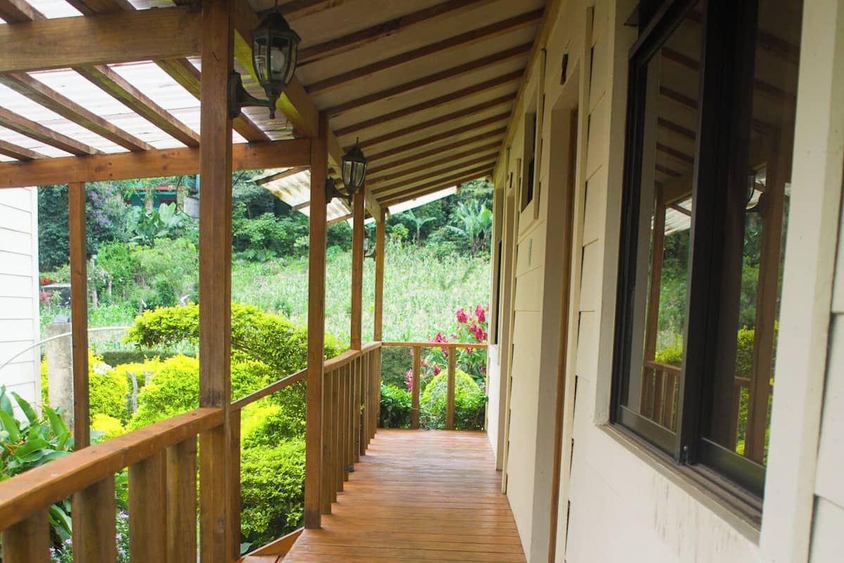 A wooden covered walkway with a railing, leading to a white building with windows.