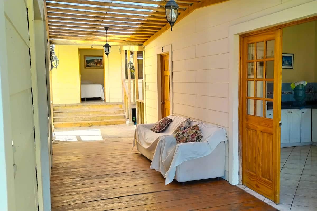 A corridor with a wooden floor leading to a room with a white couch and a wooden door.
