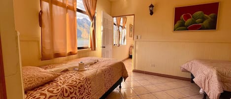 A hotel room with two beds, a view of the mountains through the window, a painting on the wall, and a ceiling fan.