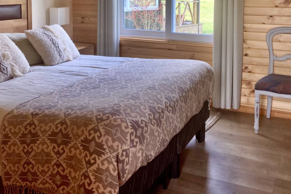 Un dormitorio con una cama grande, paredes de madera, una ventana con cortinas y vistas al exterior.