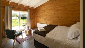 Un dormitorio con una cama grande, paredes de madera, una ventana con cortinas, una mesita pequeña y una silla.