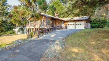 A two-story wooden house with a garage, a balcony, and a driveway leading to the front door.