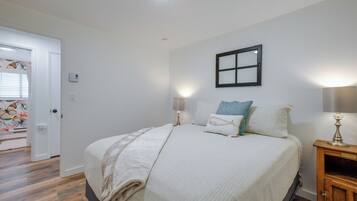 A bedroom with a bed, bedside lamps, a nightstand, a window with blinds, and a door.