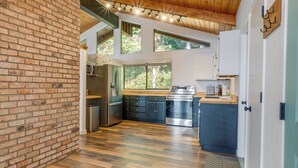 Une cuisine avec un mur en briques, un plancher en bois et une vue sur les arbres à travers de grandes fenêtres.