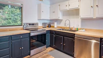 A modern kitchen with black and white cabinetry, stainless steel appliances, and a wooden countertop.
