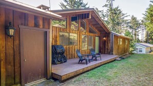 Une cabane en bois dotée d’une terrasse, de deux chaises et d’un espace barbecue couvert.