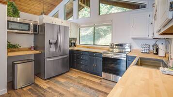 A modern kitchen with stainless steel appliances, wooden flooring, and large windows.