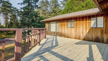 A wooden cabin with a deck, surrounded by trees.