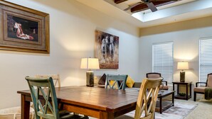 Un comedor con mesa y sillas de madera, un cuadro en la pared y dos lámparas sobre mesitas.