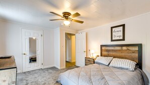 A bedroom with a bed, a ceiling fan, a framed inspirational quote, and a wooden headboard. - Steps to Crystal Lake: Spacious Retreat w/ Views (Barton)