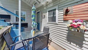 An outdoor patio with a table and chairs, a blue umbrella, and a flower arrangement on the house wall. - Steps to Crystal Lake: Spacious Retreat w/ Views (Barton)