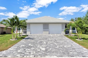 A modern building with two garage doors, a paved driveway, and palm trees. - "Everglade Kiss" 3bedroom 2bath 65in tv, BBQ, 16 jets hot tub, playground (Port Charlotte)