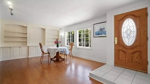 A spacious room with a wooden floor, a dining table with chairs, a wooden door, and a window with a view of greenery. - Casa De for 8people/3BD 3BA, 10people/3BD 4BA,+12people/4BD 4BA (Thousand Oaks)