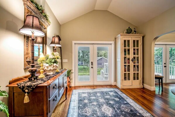A spacious entryway with a wooden floor, a large rug, a cabinet with glass doors, and a door leading to a covered porch.