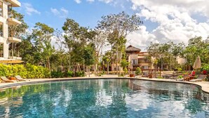A clear swimming pool surrounded by lounge chairs and a tropical garden. - RELAX TULUM apartment, 2 bedrooms with a huge 4000 ft rooftop, pools, BBQ, and jungle view (Tulum)