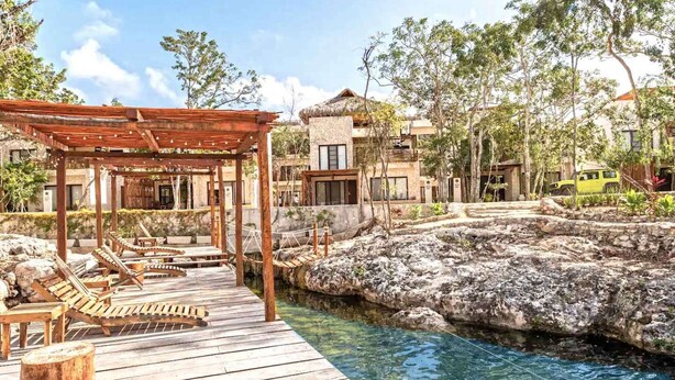 A wooden deck with lounge chairs, a pergola, and a clear pool surrounded by rocky terrain and trees. - RELAX TULUM apartment, 2 bedrooms with a huge 4000 ft rooftop, pools, BBQ, and jungle view (Tulum)