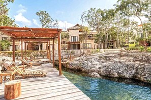 A wooden deck with lounge chairs, a pergola, and a clear pool surrounded by rocky terrain and trees. - RELAX TULUM apartment, 2 bedrooms with a huge 4000 ft rooftop, pools, BBQ, and jungle view (Tulum)
