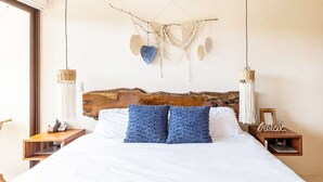 A bedroom with a wooden headboard, white bedding, two blue pillows, a macrame wall hanging, and two wall-mounted lamps. - RELAX TULUM apartment, 2 bedrooms with a huge 4000 ft rooftop, pools, BBQ, and jungle view (Tulum)