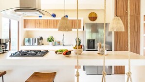 A modern kitchen with a central island, stainless steel appliances, and a hanging light fixture. - RELAX TULUM apartment, 2 bedrooms with a huge 4000 ft rooftop, pools, BBQ, and jungle view (Tulum)