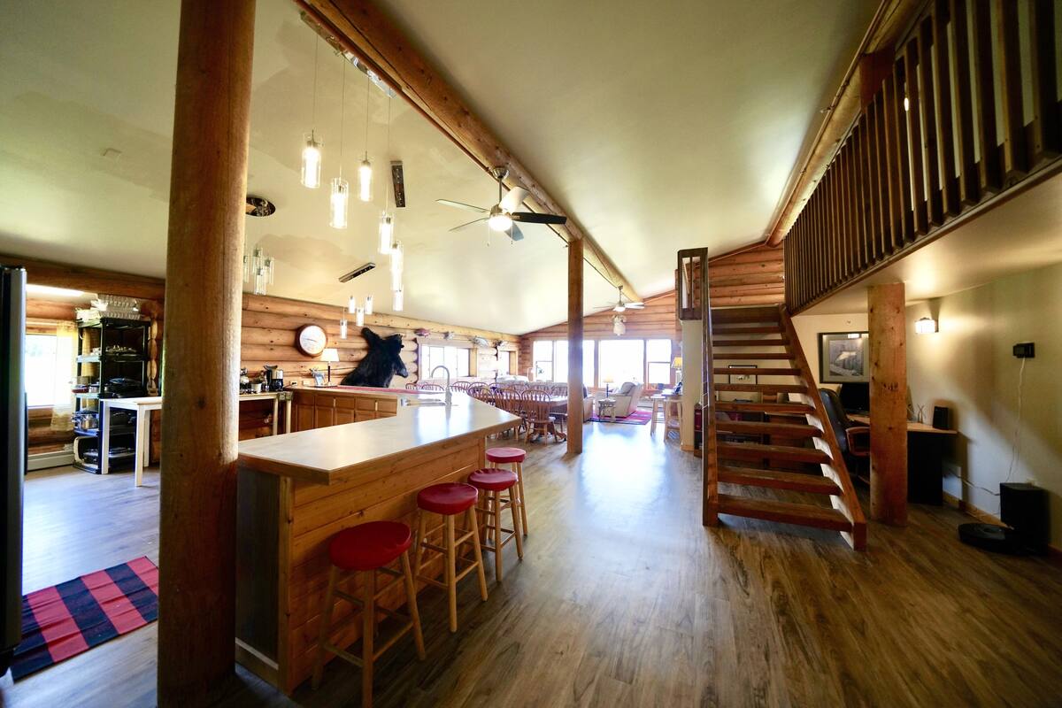 A spacious kitchen with wooden bar stools, a large island, and a staircase leading to an upper level.