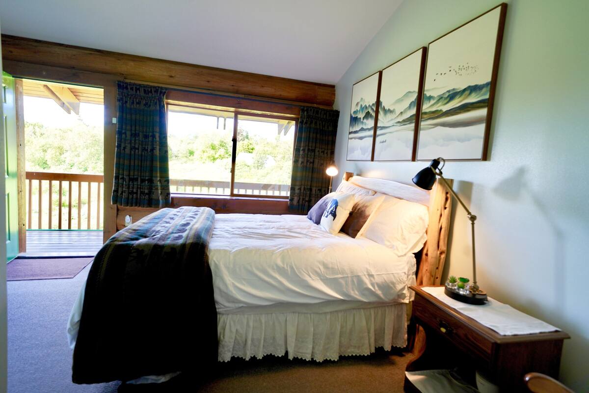 A bedroom with a bed, a nightstand, a lamp, and a view of the outdoors through a sliding door.