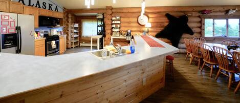 Une cuisine spacieuse dotée de meubles en bois, d’un grand îlot central avec un évier et d’un coin repas avec des chaises en bois.