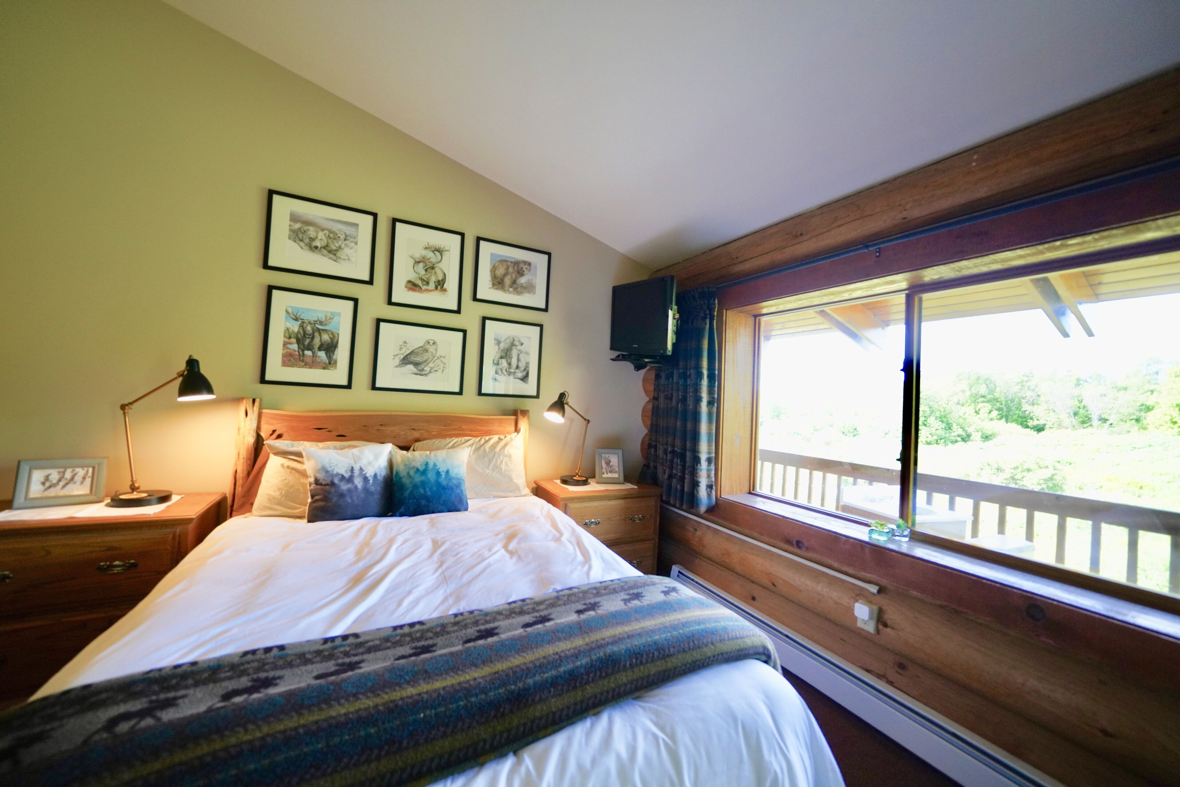 A bedroom with a bed, bedside tables, a window with a view, and framed pictures on the wall.