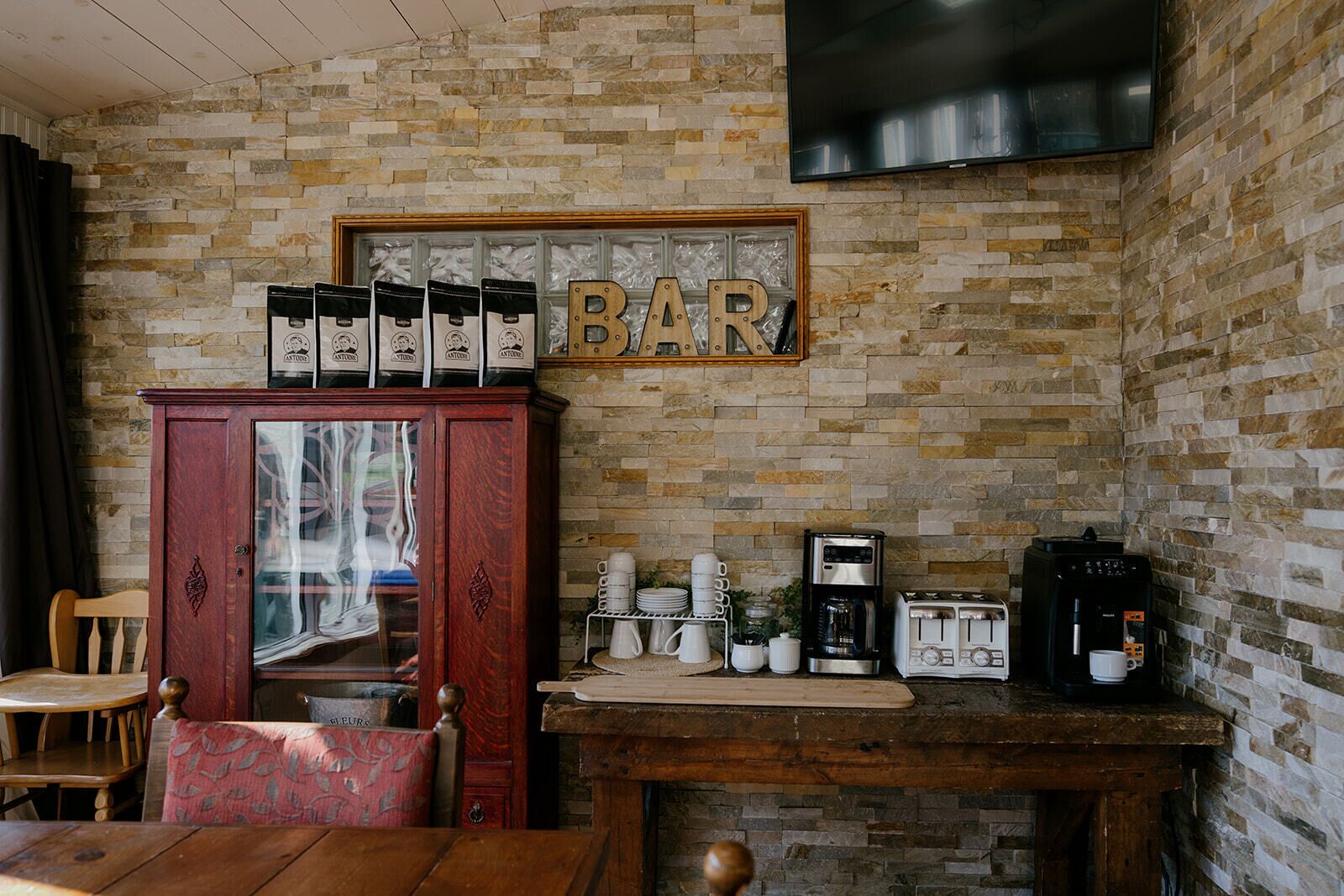 Une cuisine rustique avec un mur en pierre, un meuble en bois contenant des machines à café, une machine à café, un grille-pain et une enseigne de bar au-dessus du comptoir.