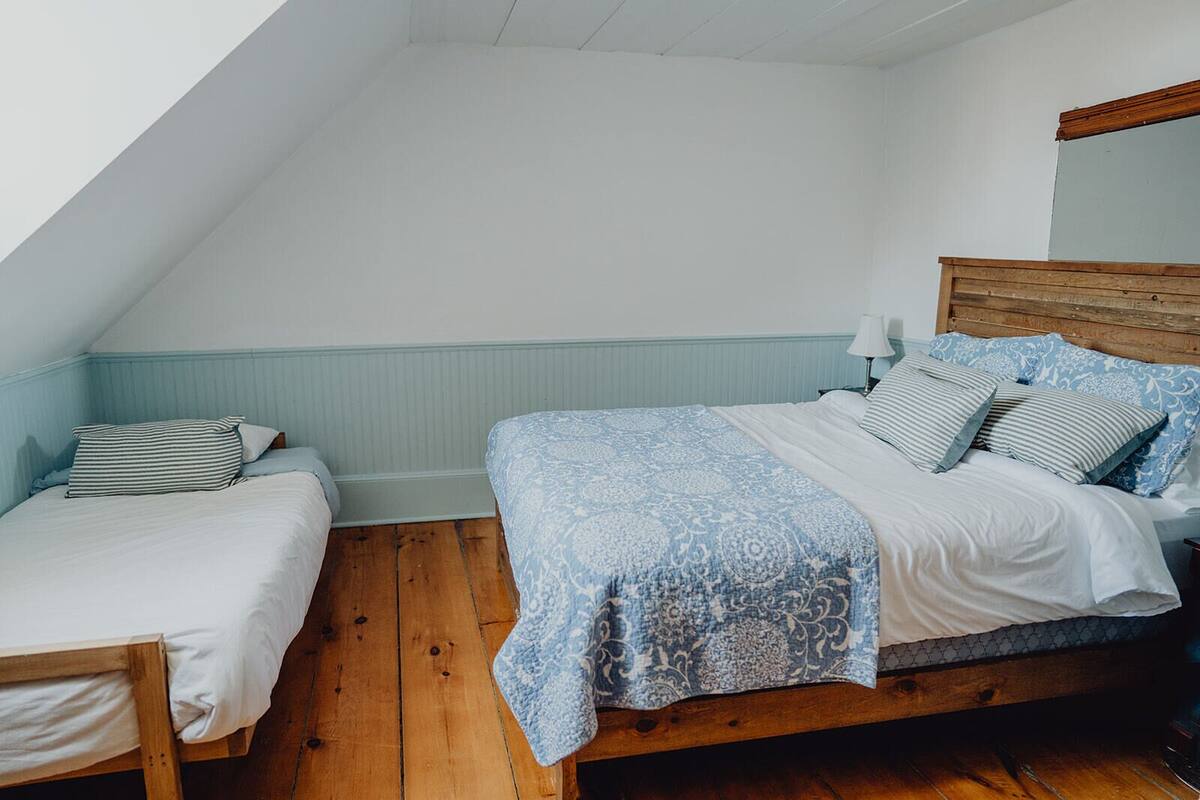 A bedroom with two beds, wooden flooring, and a sloped ceiling.