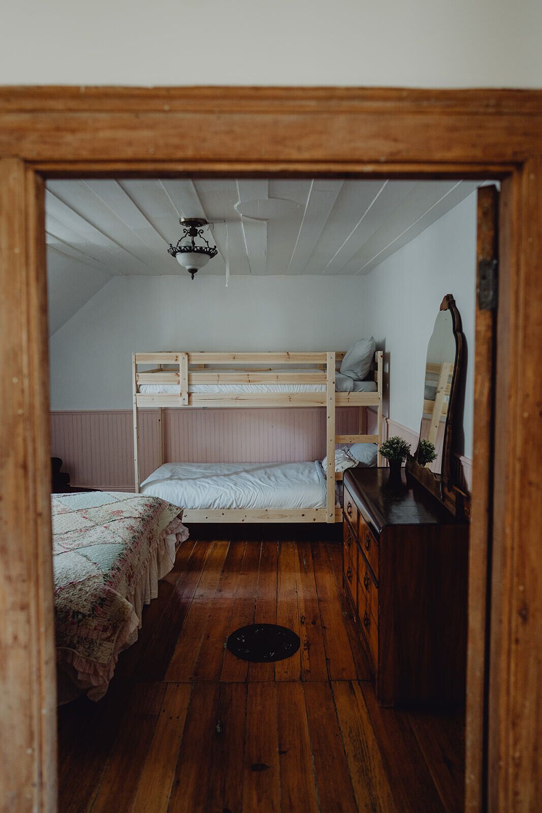 Una habitación pequeña y acogedora con una cama litera, un aparador y un espejo.