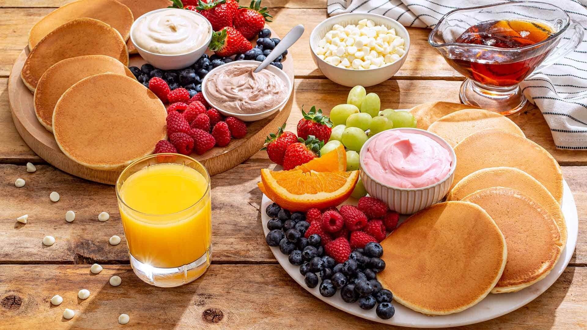 A breakfast spread with pancakes, berries, and a glass of orange juice on a wooden table.